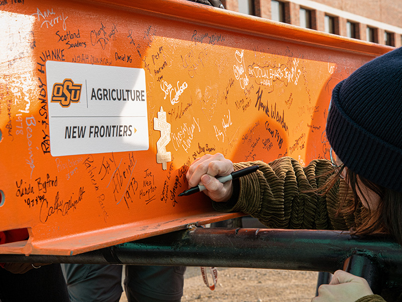 Student signing an orange construction beam