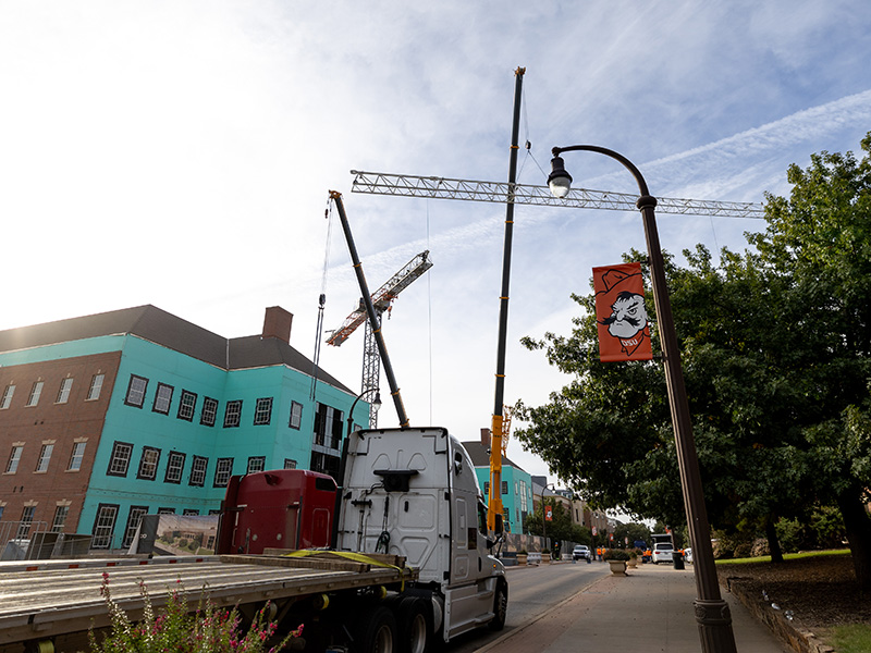 A crane and a semi truck in front of a building site. 