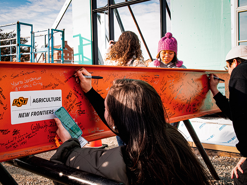 Five students signing an orange construction beam
