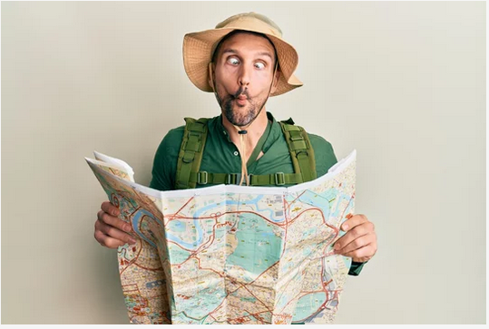 A person wearing a hat, making a funny face while reading a map.